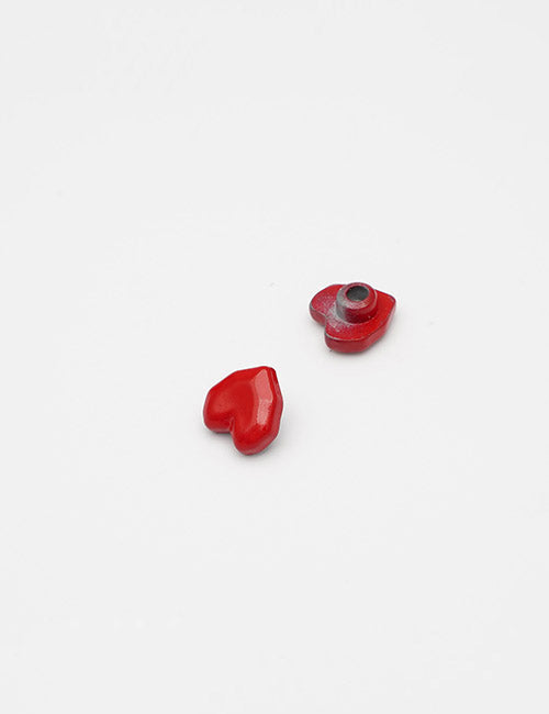Two small, red, heart-shaped Adornments by YIPAI are shown on a plain white surface. One features a round metallic hole in the center, while the other is solid.