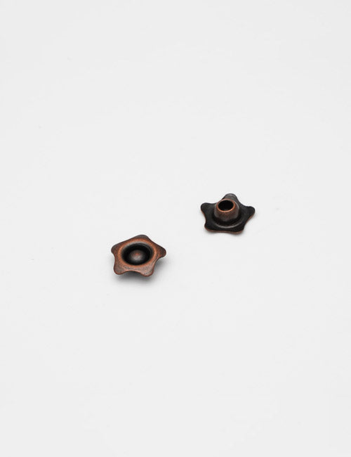 Two small, star-shaped Adornments by YIPAI with a central hole and dark metallic finish, displayed on a plain white background.