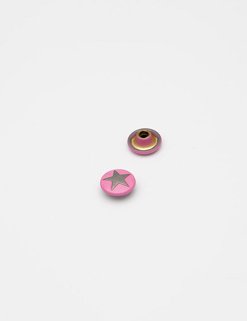 Two small round Adornments by YIPAI are shown on a white background: one is pink with a gray star, while the other displays its gold metal backing.