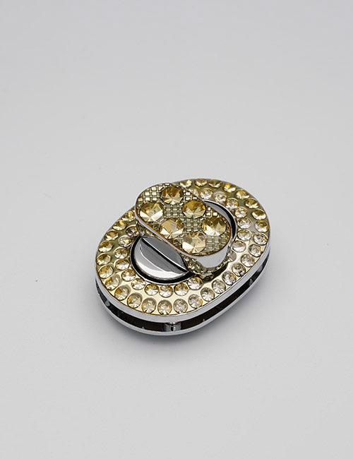 YIPAI Closures: Oval-shaped metallic closure adorned with small yellow gemstones, featuring a smaller matching oval on top, displayed against a plain gray background.