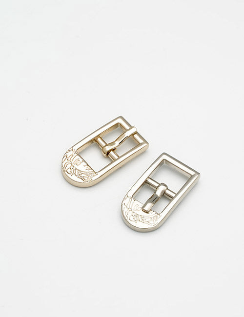 Two YIPAI Buckles, one gold and one silver, both with engraved floral designs on the lower part, are placed side by side on a plain white background.