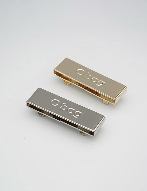 Two rectangular YIPAI Buckles, one gold and one silver, both engraved with O bag, are placed side by side on a plain light surface.