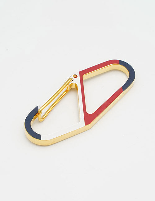 YIPAIs Chains: a gold carabiner with geometric design, accented by navy blue, white, and red enamel on a white background.