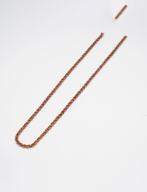 A YIPAI Chains copper-colored necklace rests on a white surface, its clasped ends broken and detached from the main chain length.