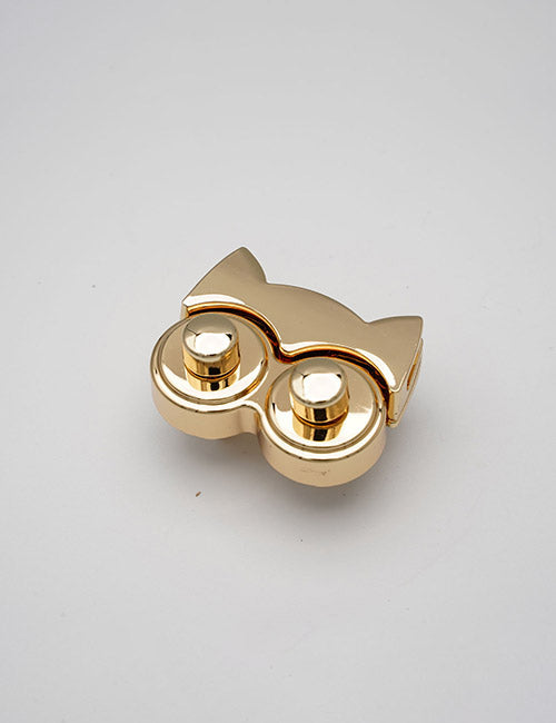 A small, gold metallic YIPAI Closures shaped like cat ears atop two raised circular buttons, resembling a stylized cat face, is displayed on a plain white background.