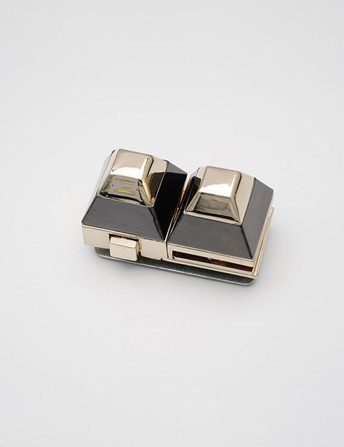 A small, vintage YIPAI Closures item with two raised square buttons side by side, featuring a shiny silver and black finish, displayed on a plain white background.