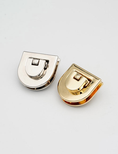 Two YIPAI Closures, one in silver and one in gold, are side by side on a white background. Each has a rounded half-moon shape with a small rectangular locking mechanism.