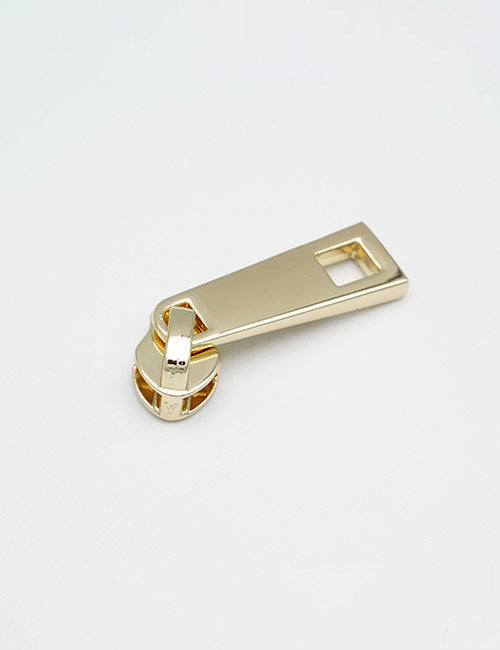 A YIPAI Fasteners gold-colored metal zipper pull tab rests on a white surface, featuring a rectangular hole at one end and a circular hinge joining its two parts.