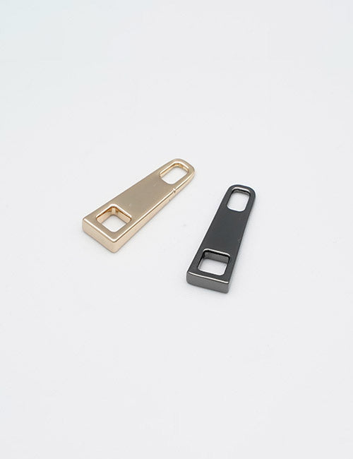 Two flat, rectangular YIPAI Fasteners zipper pulls, one gold and one black, lie on a plain white background. Each pull features a small square cutout and a rounded rectangular cutout at one end.