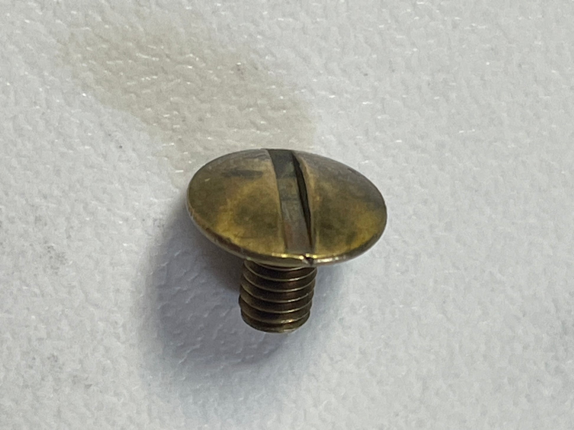 A close-up of a YIPAI Fasteners brass slotted flat-head screw with a short threaded shaft resting on a white textured surface.