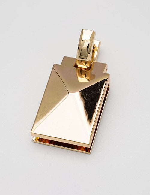 A geometric, gold-colored metal pendant called Handles by YIPAI features sharp angular facets, a rectangular shape, and a thick curved bail for attaching to a chain, shown against a plain white background.