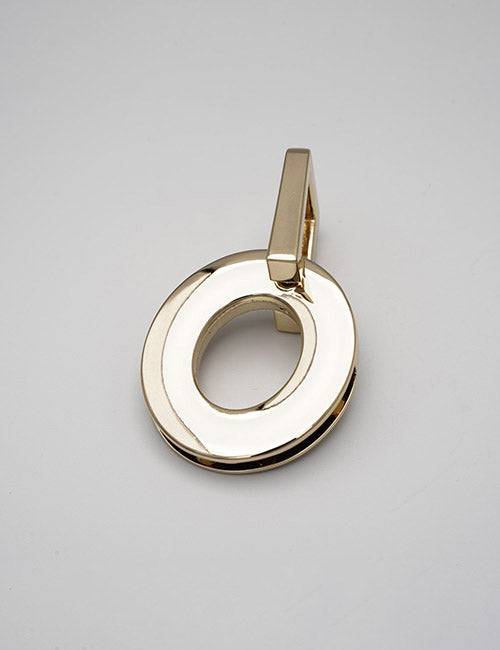 A shiny, gold-colored YIPAI Handles pendant, shaped like an irregular oval with a cut-out center and a rectangular bail at the top, rests on a plain light gray background.