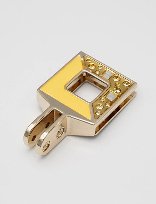 The YIPAI Handles is a gold metal hair clip with a geometric square design, yellow enamel accents, and small embedded gemstones, displayed on a plain light background.