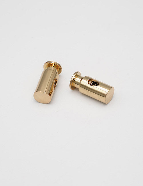 Two small, cylindrical YIPAI Handles in gold metal with side holes are lying on a plain white surface.