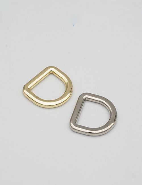 Two metal D-rings from YIPAIs Rings & Slides collection, one gold and one silver, are placed side by side on a plain light gray surface with their open sides facing downward.