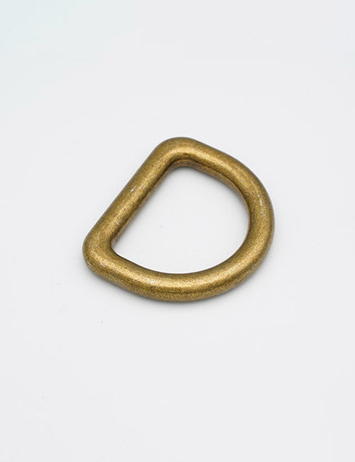 A YIPAI Rings & Slides brass D-ring with a thick, metallic finish rests on a plain white surface, featuring a semicircular shape with one straight and one curved edge.
