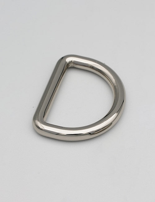 A YIPAI Rings & Slides silver metal D-ring rests on a plain light gray surface, flat side to the left and curved side to the right.