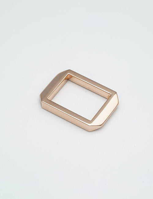 A YIPAI Rings & Slides rectangular metallic gold buckle with beveled edges rests flat on a plain, light gray surface.