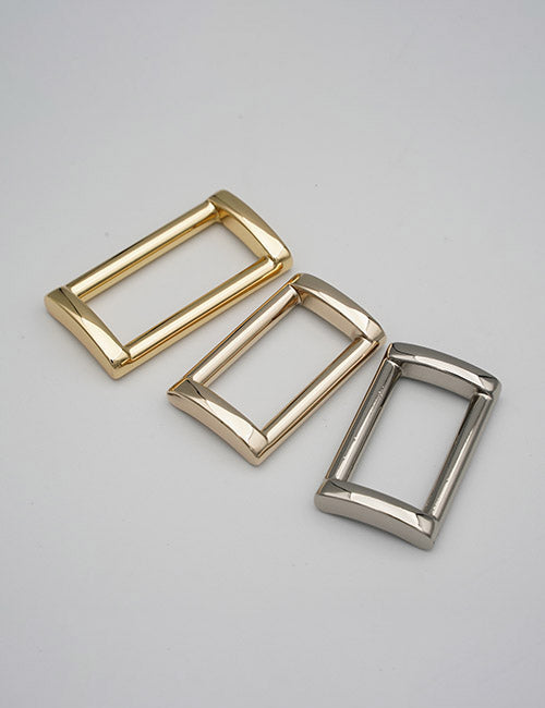 Three YIPAI Rings & Slides rectangular metal belt buckles in gold, rose gold, and silver with rounded corners and a polished finish are displayed on a plain light gray background.