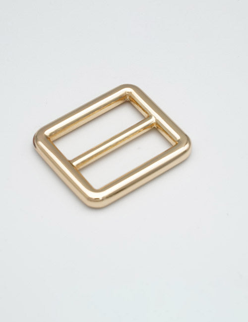 A gold rectangular metal buckle from YIPAIs Rings & Slides, featuring rounded edges and a central bar splitting it into two sections, shown lying flat on a plain light gray background.