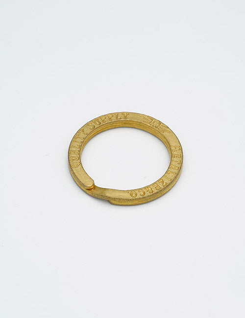 A round, brass-colored metal key ring from YIPAIs Rings & Slides collection features a small gap for attaching keys and engraved text along the edge. The ring is displayed against a plain white background.