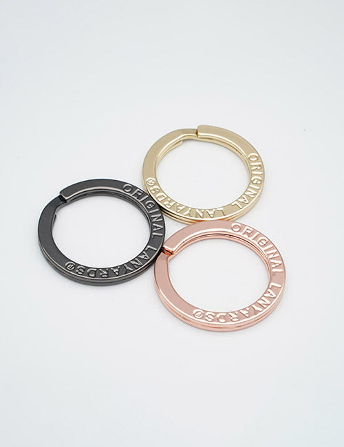 Three circular metal Rings & Slides by YIPAI—one gold, one black, and one rose gold—are arranged on a white background. Each features ORIGINAL MANA CAPS engraved around the edge.