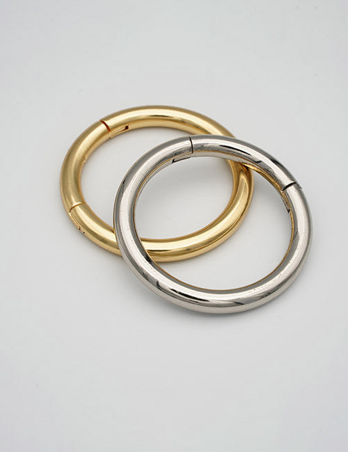 Two overlapping circular metal rings, one gold and one silver, with a smooth polished finish rest on a plain light gray background. The jewelry is from YIPAI’s Rings & Slides collection.