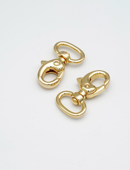 Two YIPAI Snap Hooks in shiny gold are displayed on a plain white surface, with one facing up and the other tilted to showcase their clasp and rotating base features.