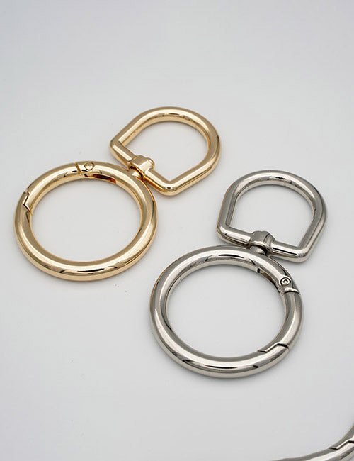 Two YIPAI Rings & Slides key rings, one gold and one silver, each featuring a round ring with a D-shaped clasp, are displayed on a plain light gray surface.